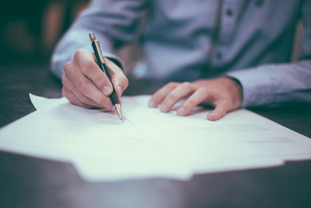 a person signing a written contract with a pen